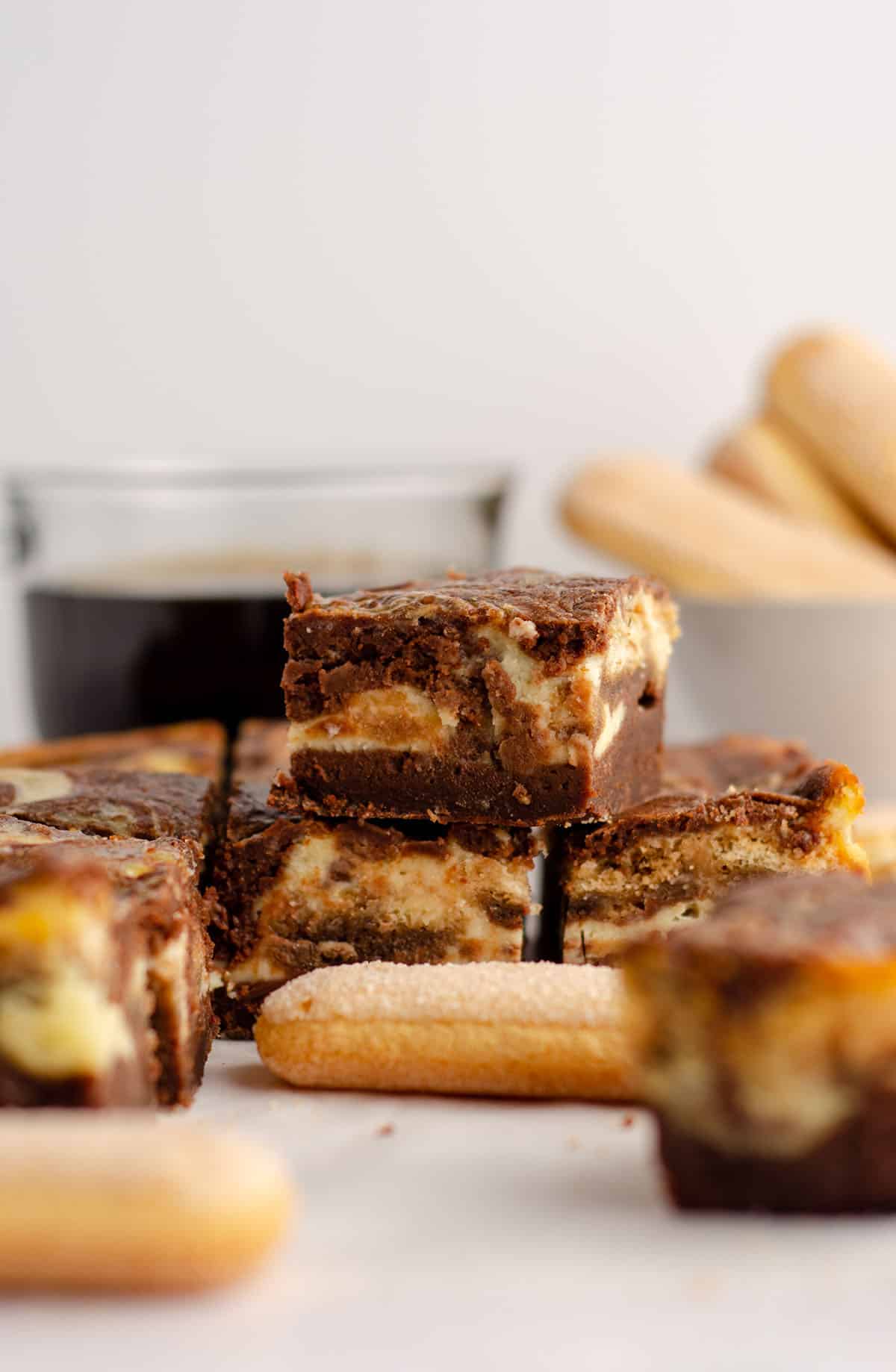 stack of tiramisu brownies with a cup of coffee and ladyfingers in the background