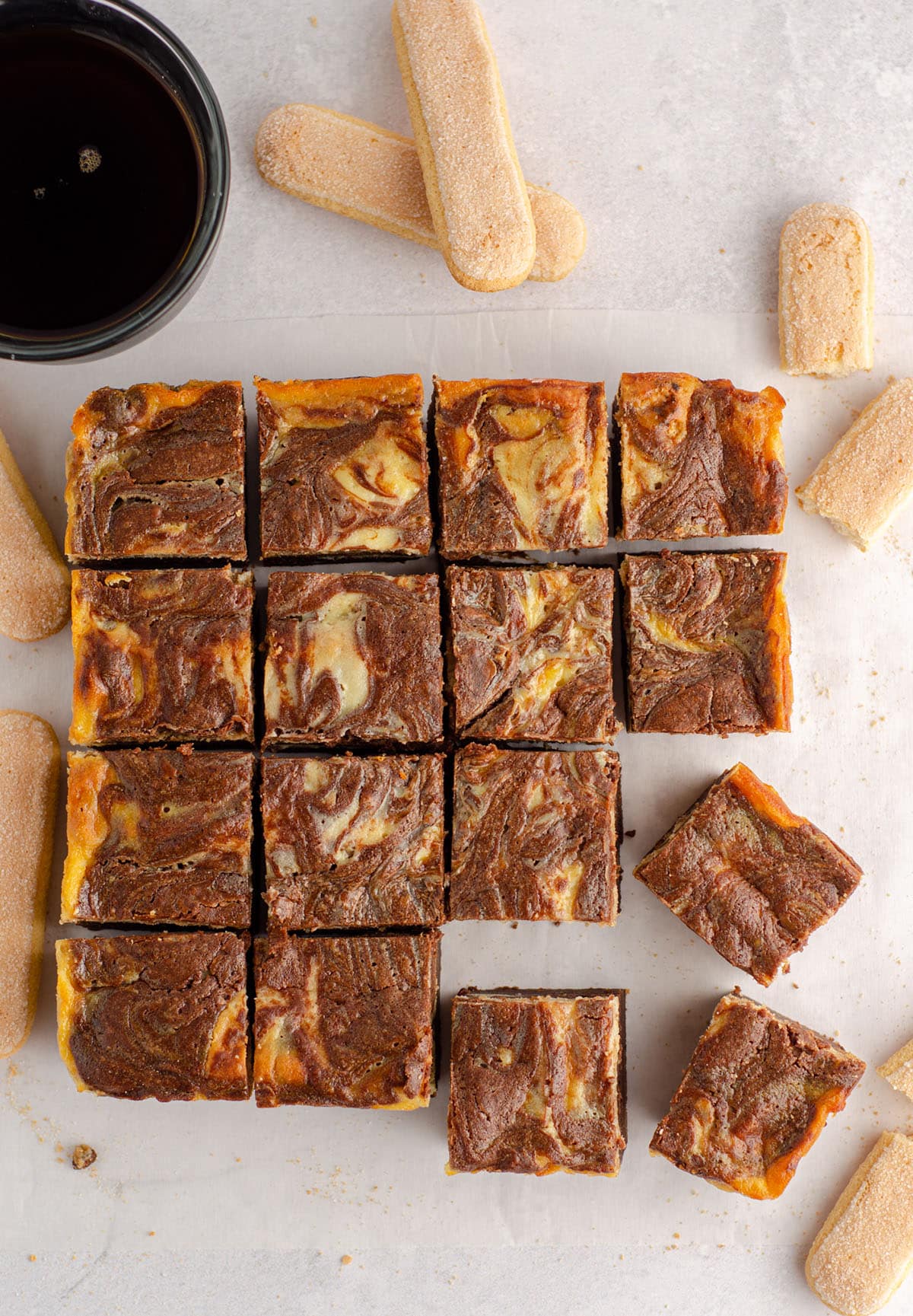 aerial photo of sliced tiramisu brownies on parchment paper with a cup of coffee and ladyfingers