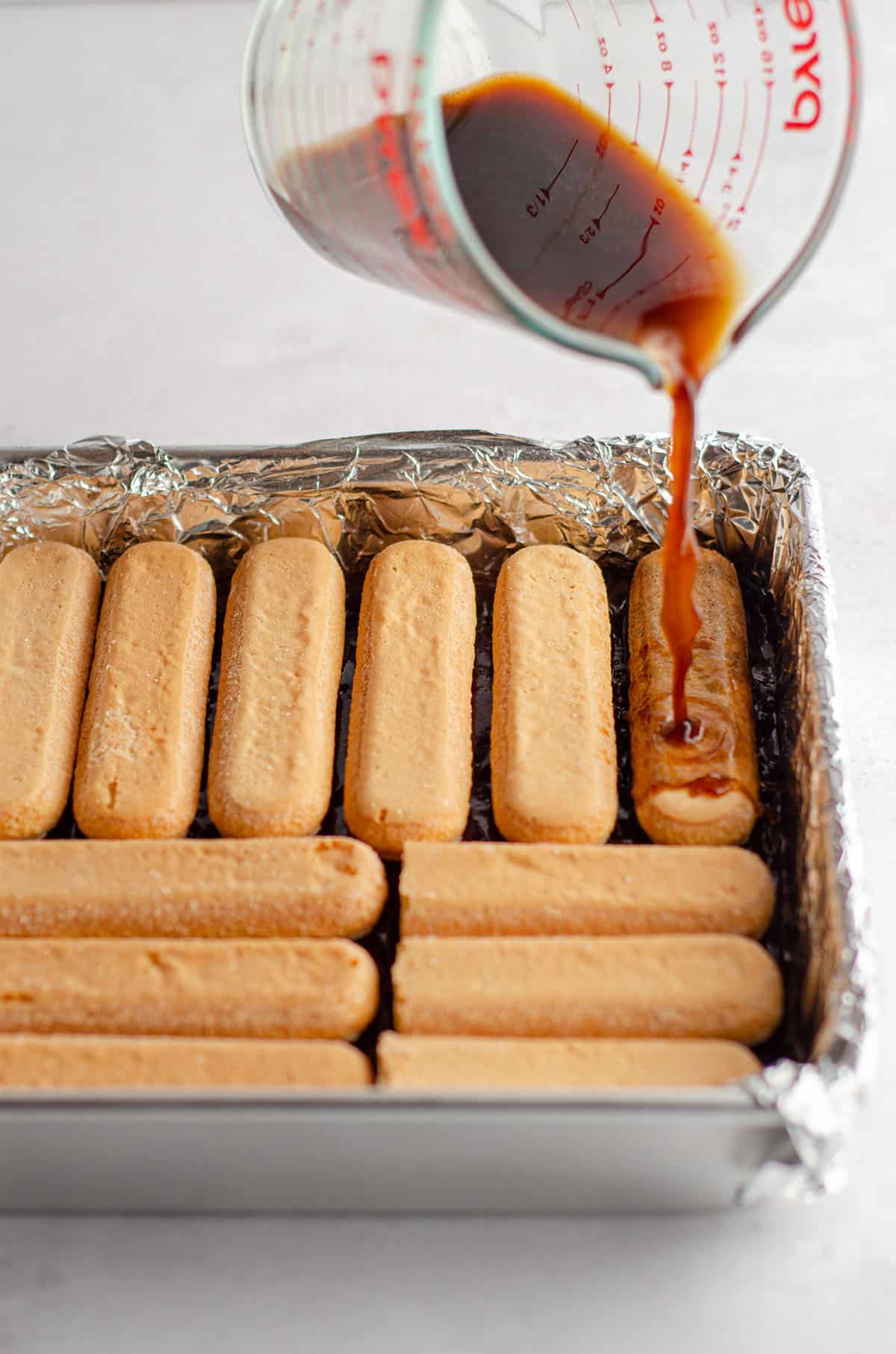 pouring coffee onto ladyfingers as a layer in the middle of tiramisu brownies