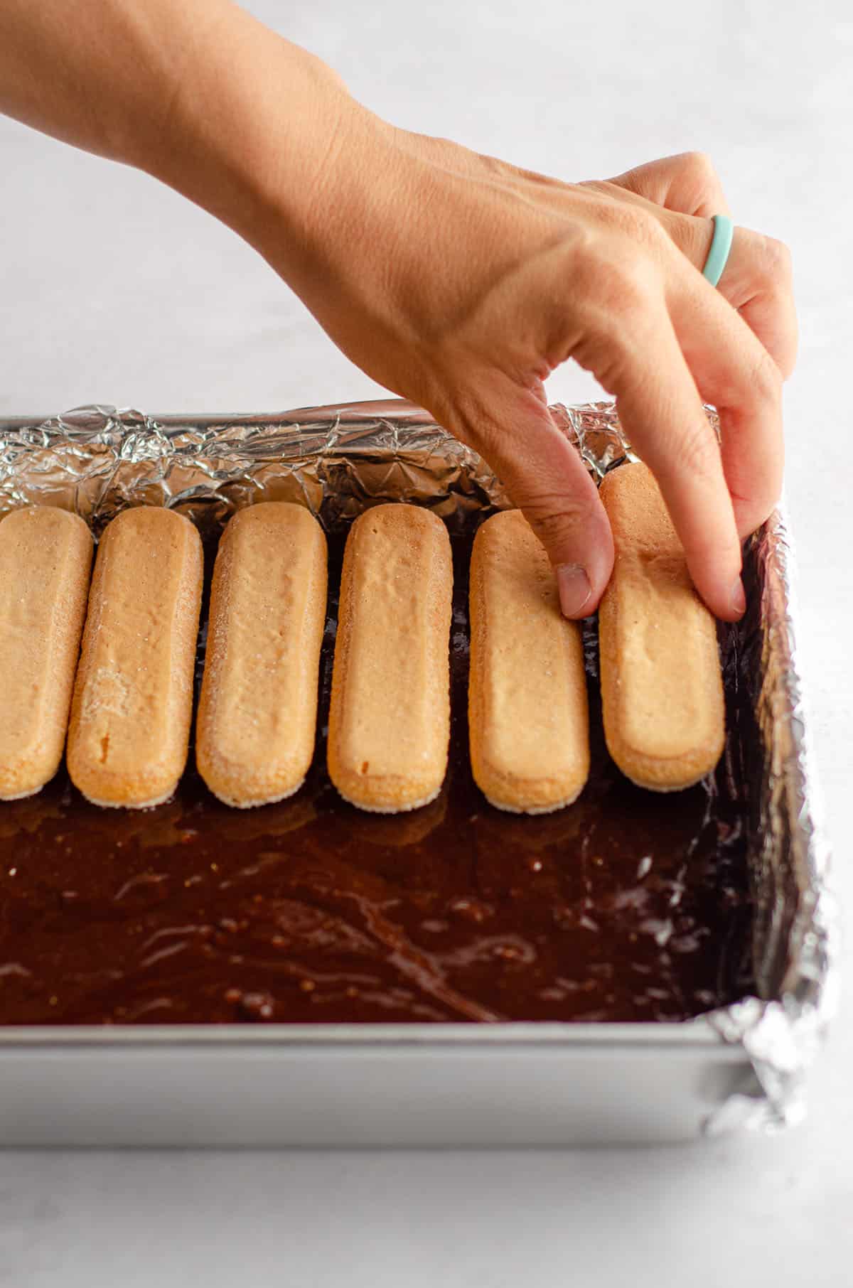 a hand layering ladyfingers into brownie batter to make tiramisu brownies