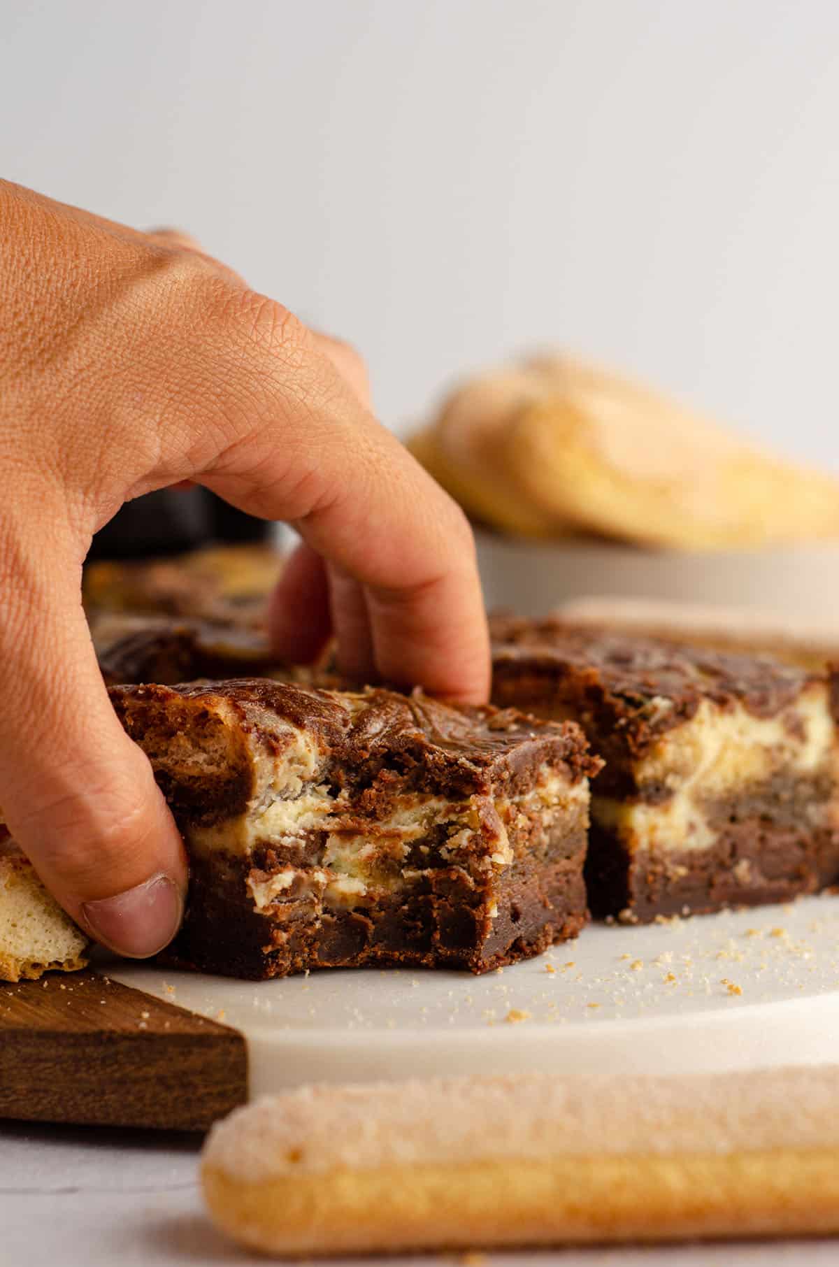 a hand grabbing a tiramisu brownie from a platter with a bite taken out of it
