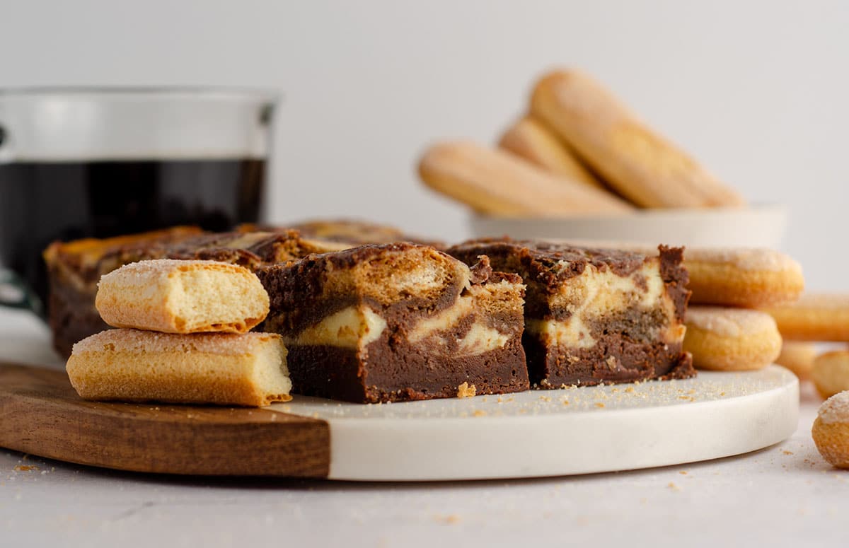 tiramisu brownies on a platter with a cup of coffee and ladyfingers in the background