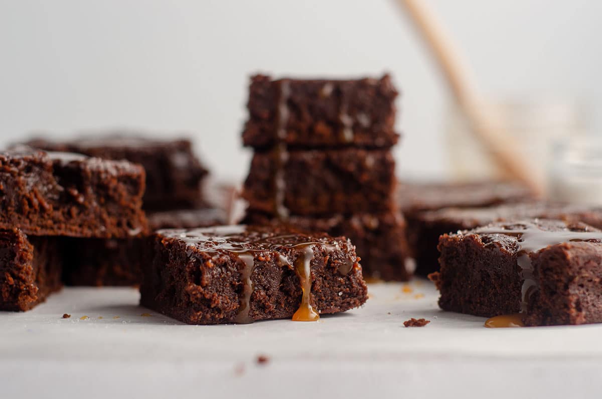 salted caramel brownie with caramel sauce dripping off of it with a stack of brownies in the background