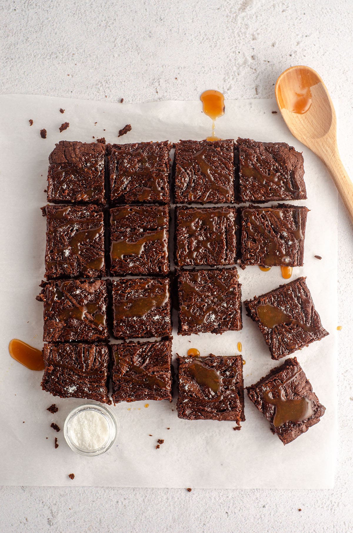 aerial photo of sliced salted caramel brownies with a little jar of sea salt and a spoon with caramel sauce dripping off of it