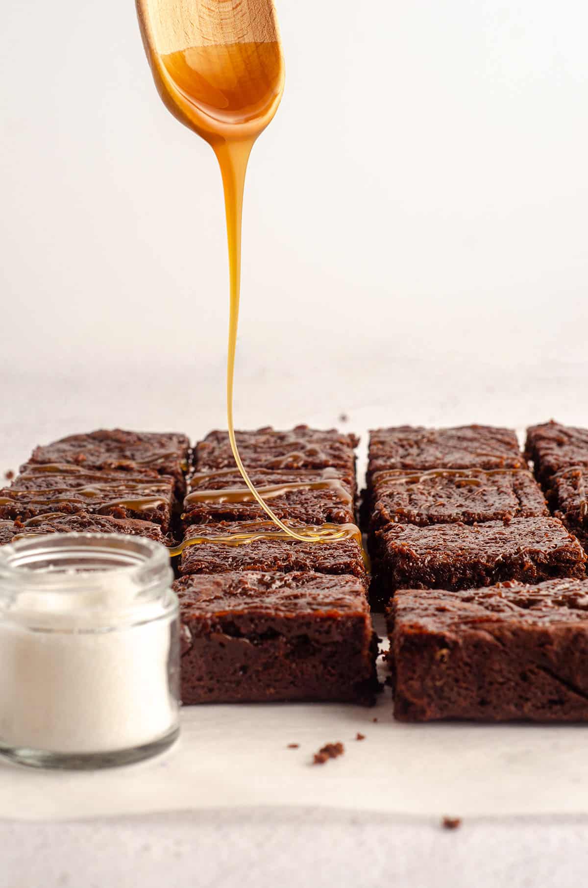 wooden spoon dripping caramel sauce onto salted caramel brownies 