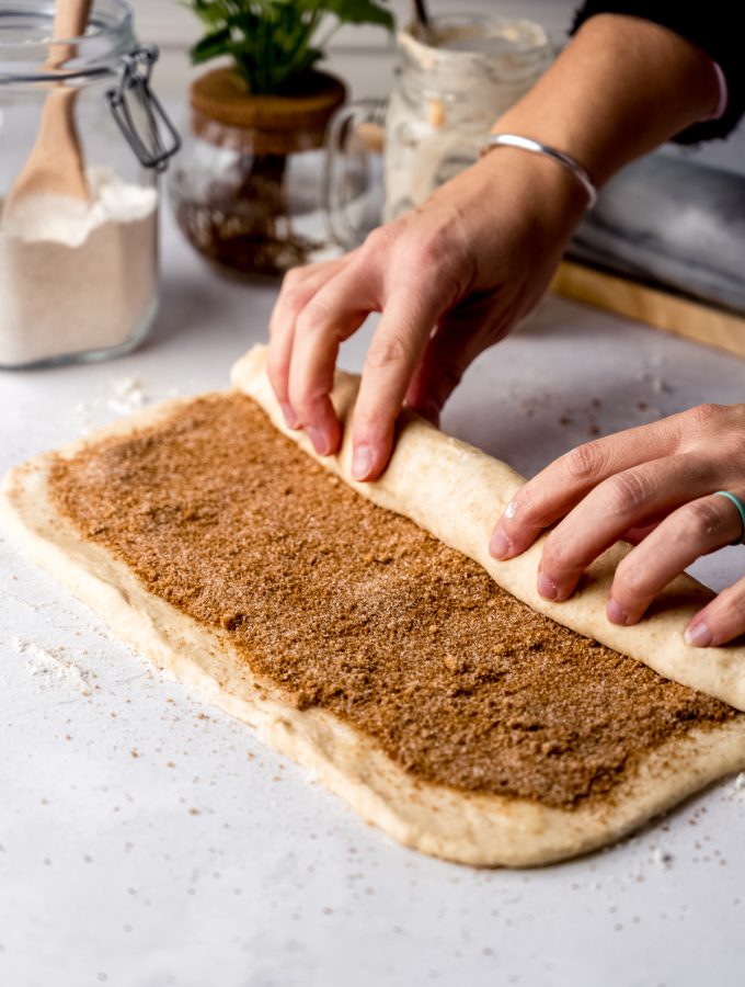 Someone is rolling up cinnamon roll dough.