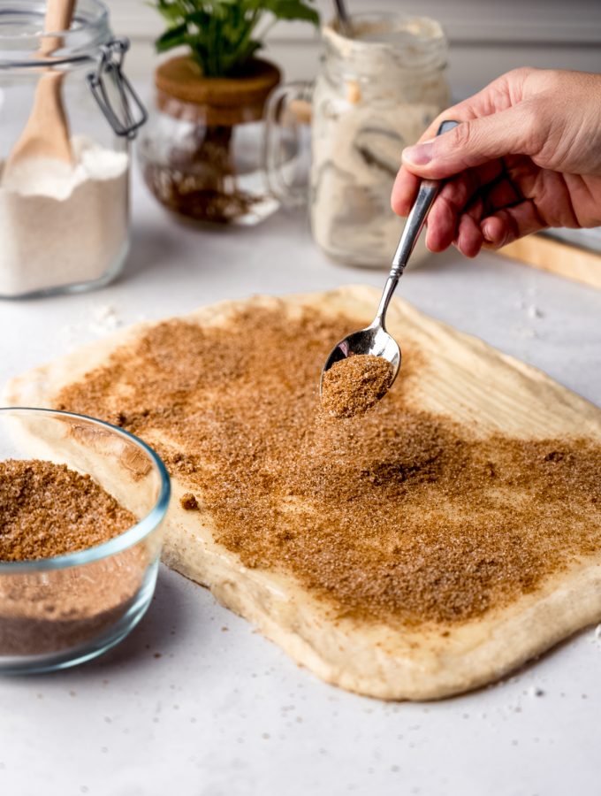 Someone is sprinkling cinnamon sugar onto a rectangle of cinnamon roll dough.