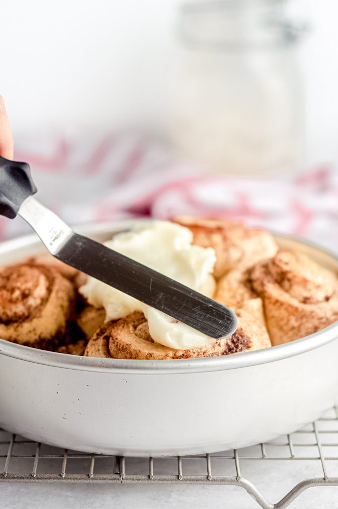 spreading cream cheese frosting on a batch of sourdough cinnamon rolls