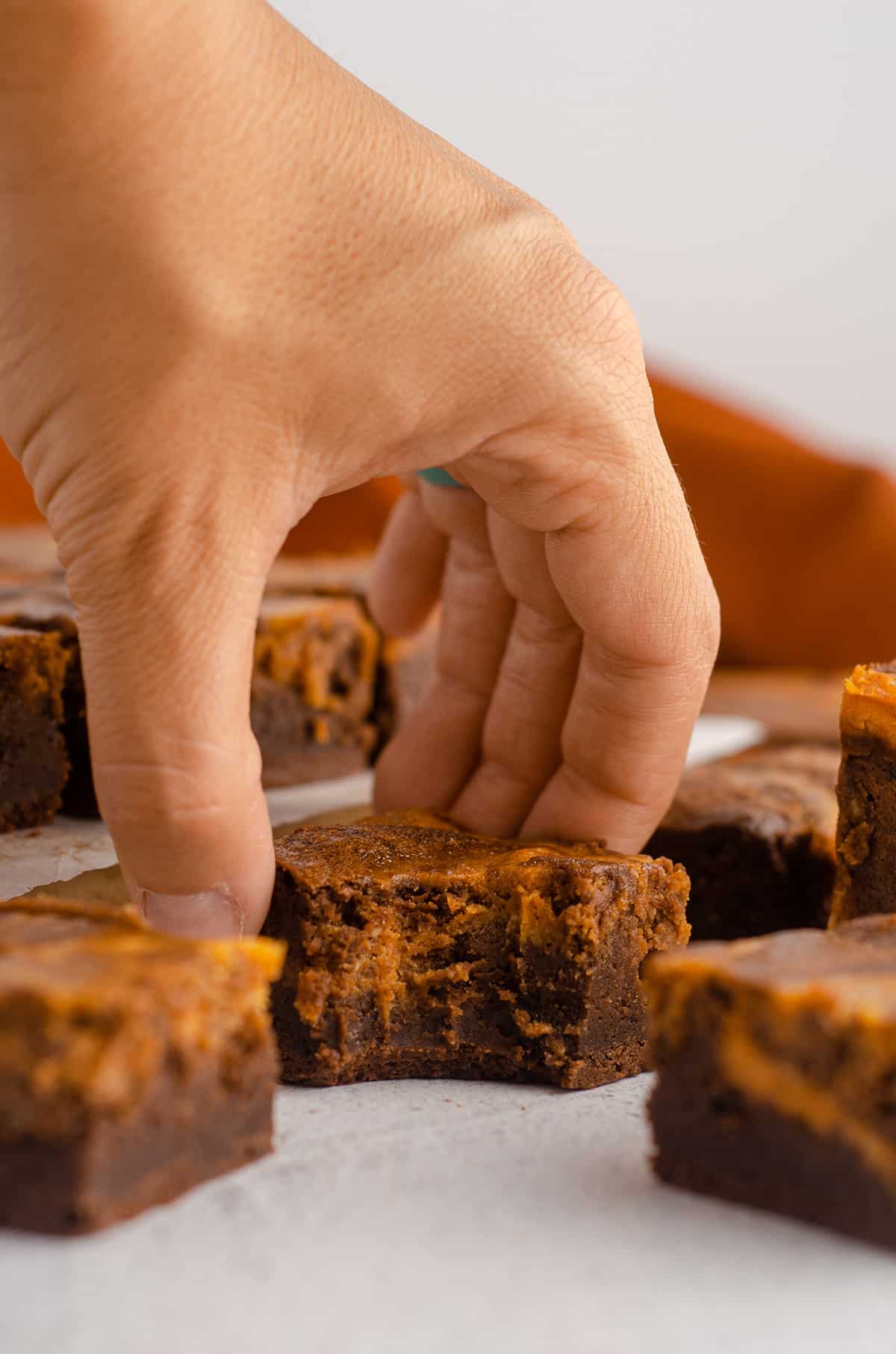 hand grabbing a pumpkin cheesecake brownie with a bite taken out of it