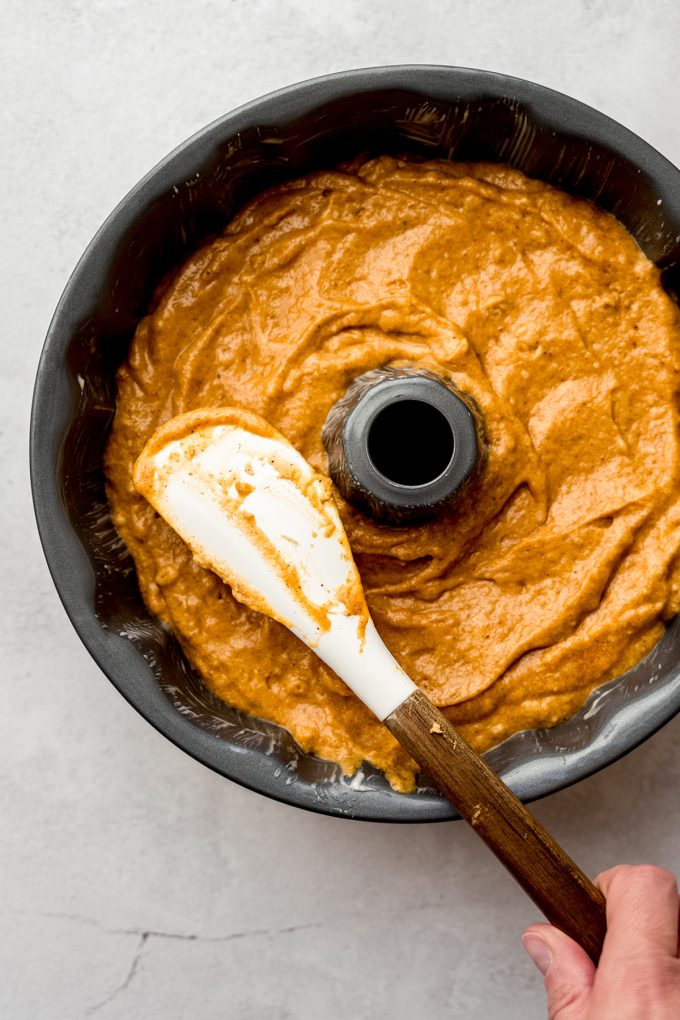 Aerial photo of pumpkin Bundt cake batter in a Bundt pan and a spatula smoothing out the batter.