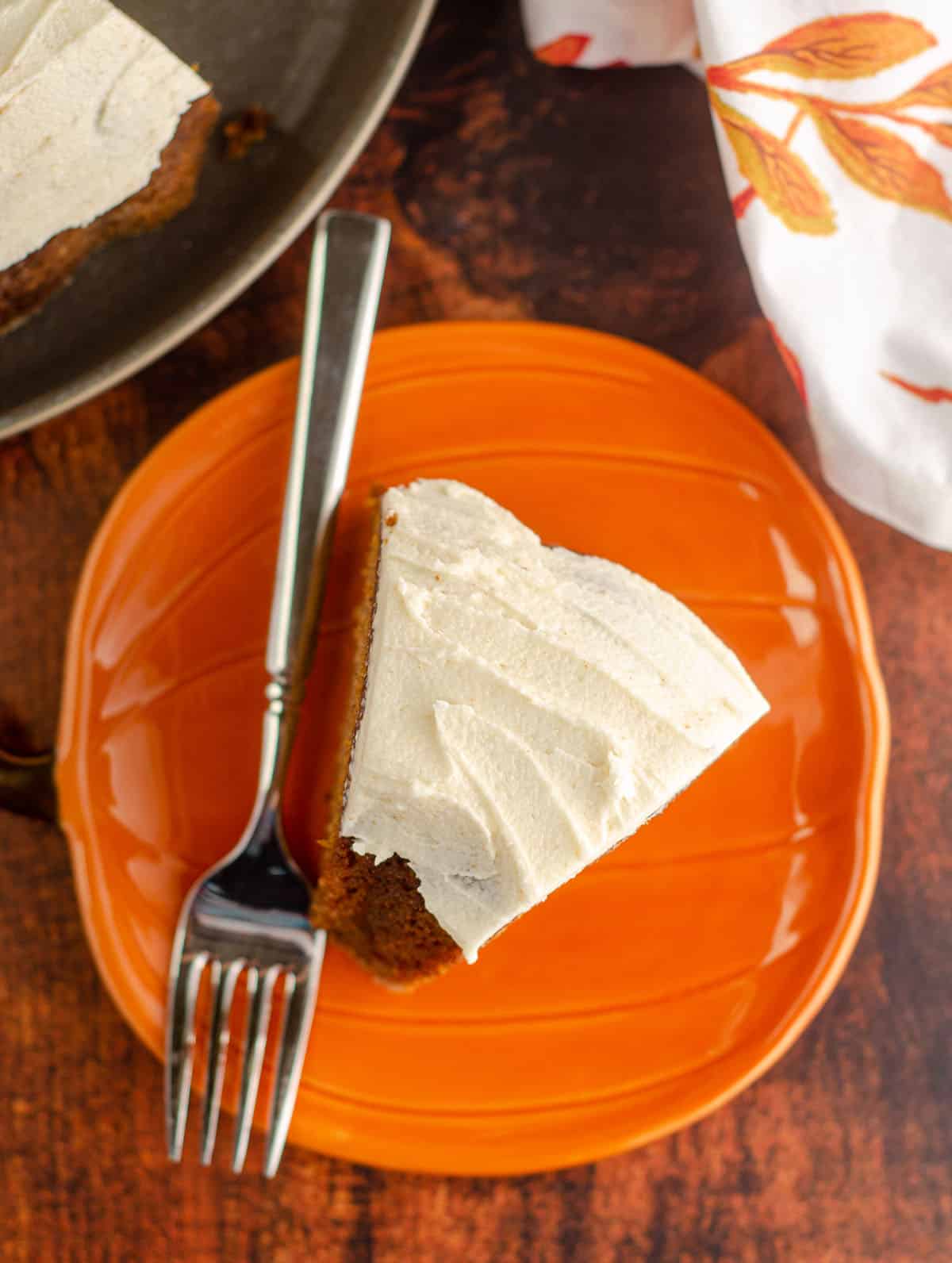 aerial photo of a slice of pumpkin bundt cake with browned butter buttercream sitting on an orange pumpkin plate