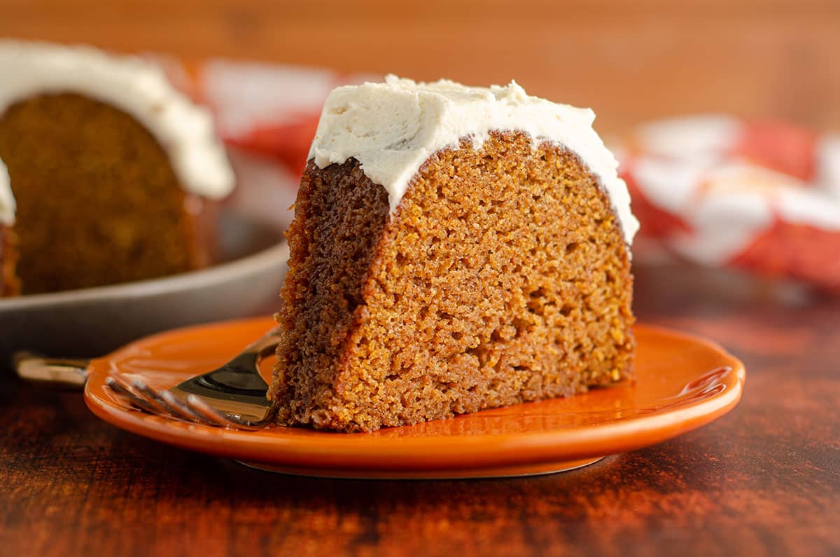 slice of pumpkin bundt cake with browned butter buttercream sitting on an orange plate