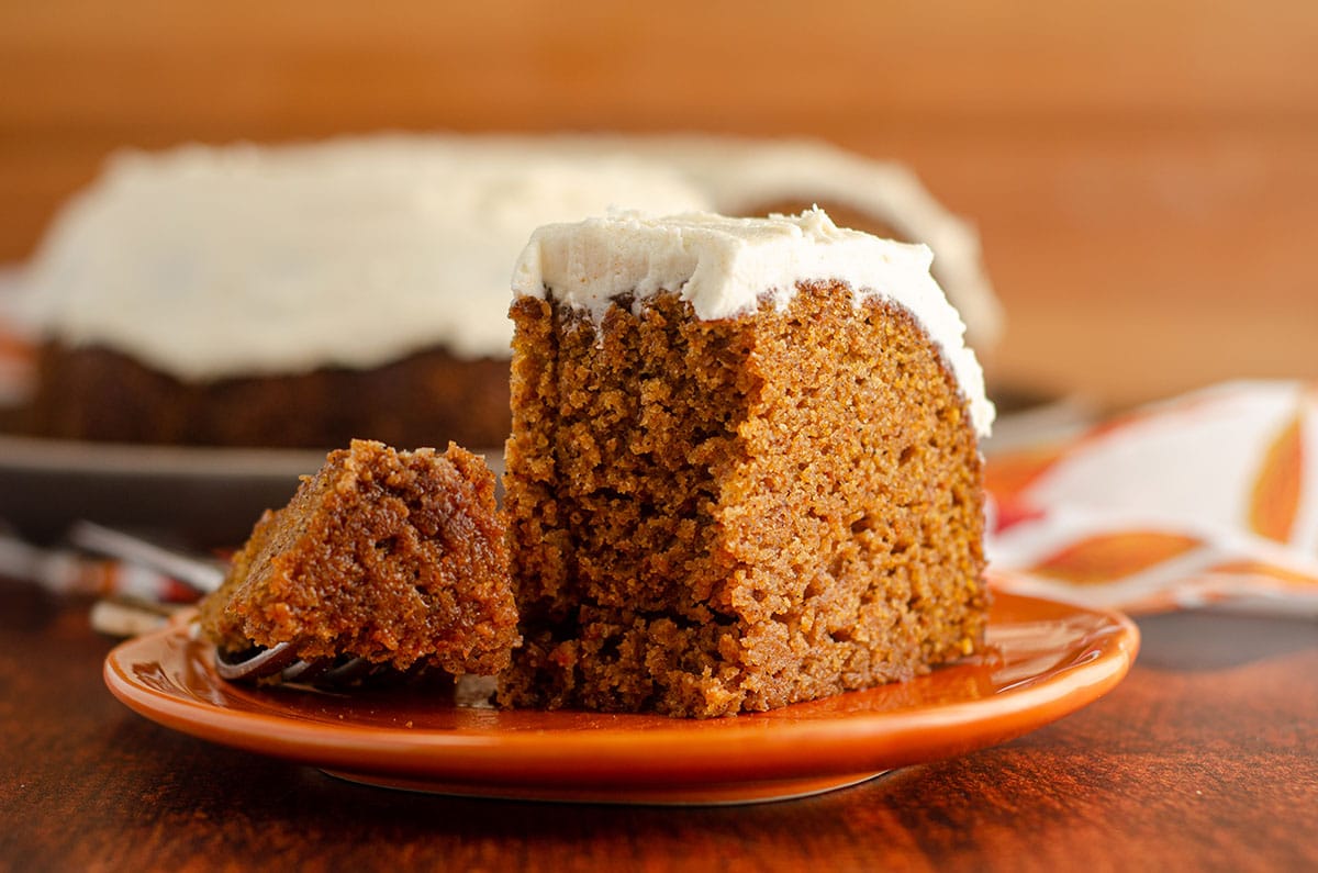 pumpkin bundt cake sitting on an orange pumpkin plate with a bite taken out with a fork