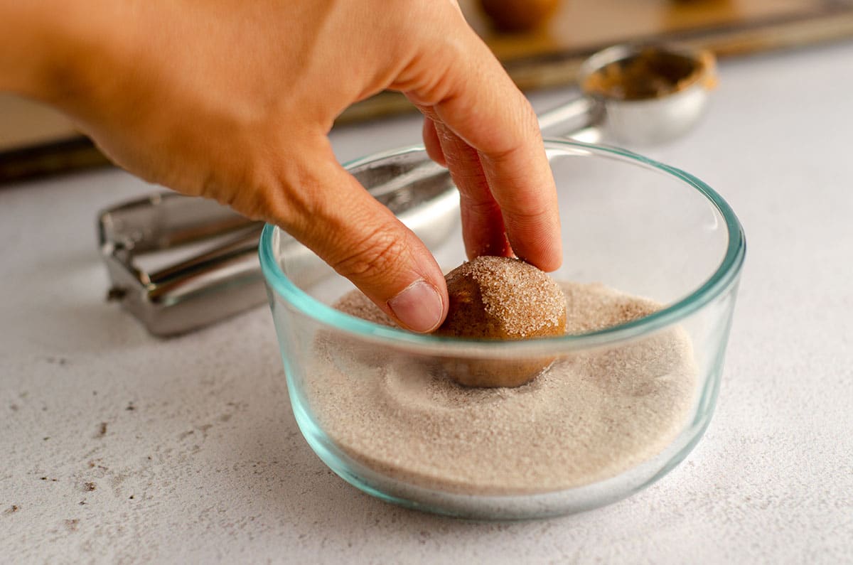 hand rolling a pumpkin spice cookie dough ball in cinnamon sugar