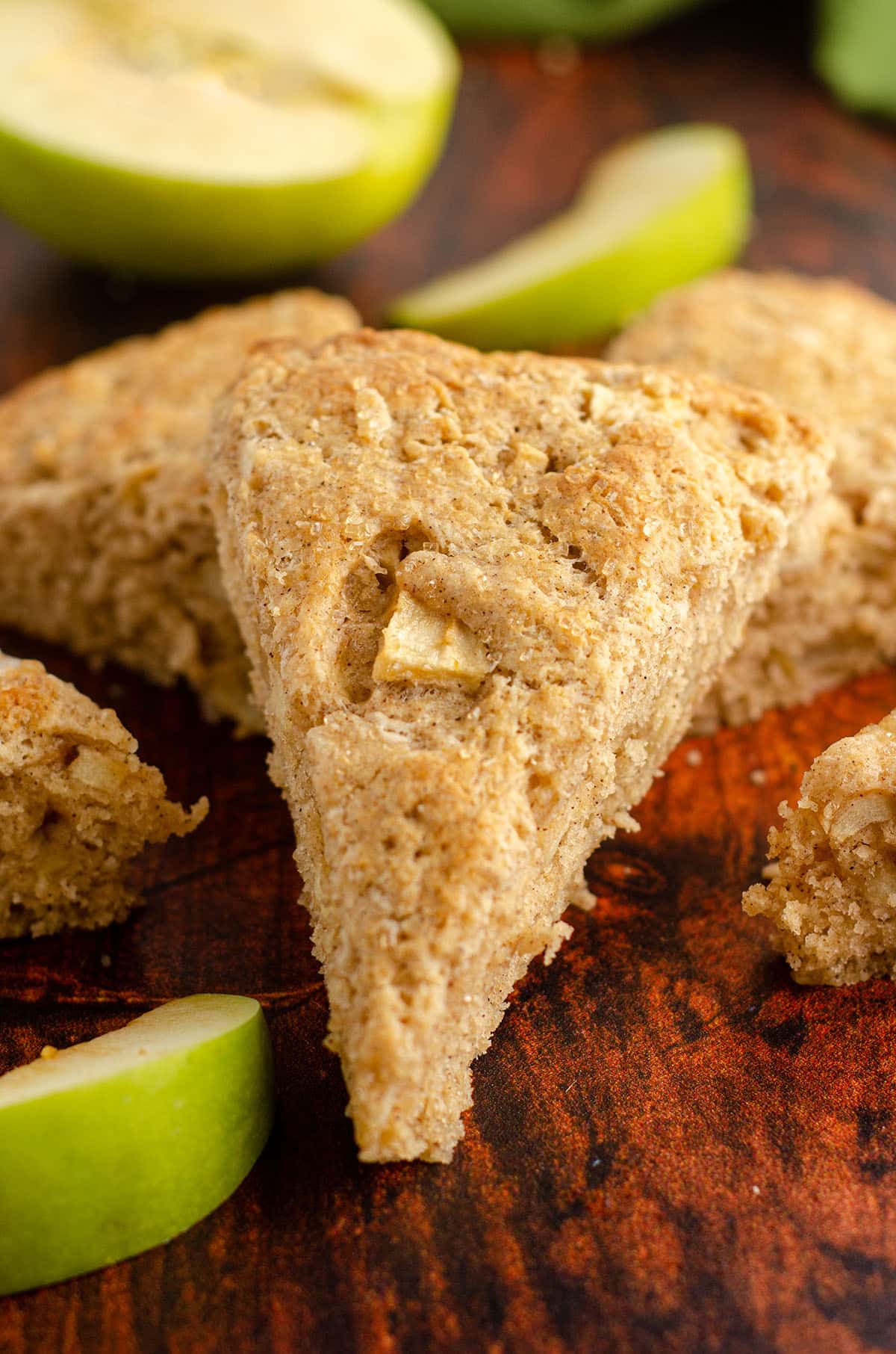 apple scone propped up on a plate with granny smith apple slices in foreground and background