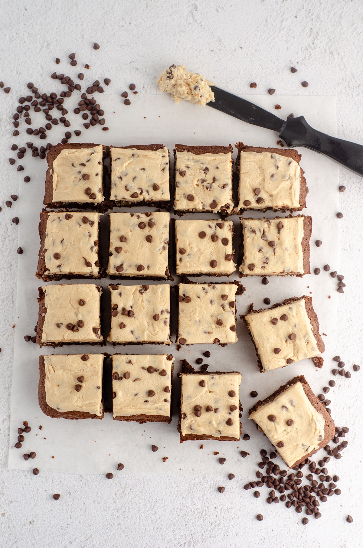 aerial photo of cookie dough brownies with cookie dough buttercream, scattered with mini chocolate chips and a spatula with buttercream on it