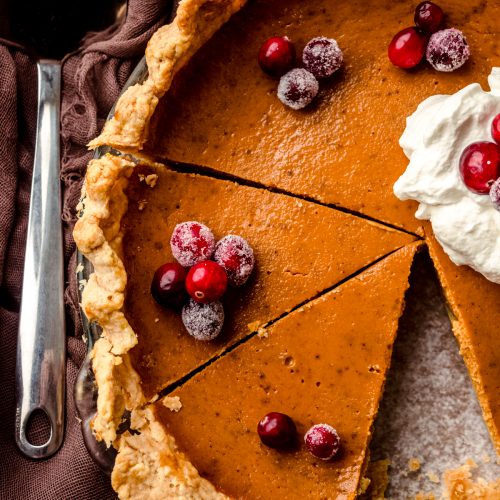 A pumpkin pie that has been cut into slices with whipped cream an cranberries on top.