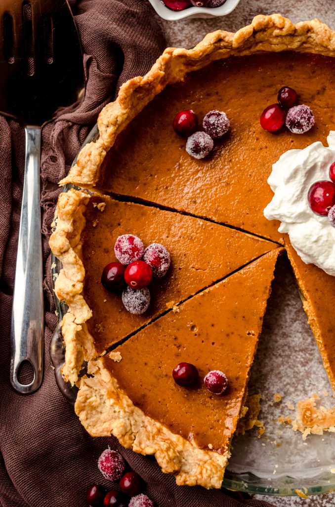 A pumpkin pie that has been cut into slices with whipped cream an cranberries on top.