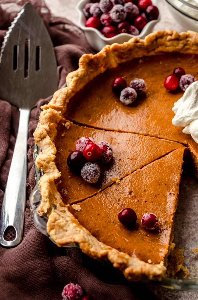 A pumpkin pie that has been cut into slices with whipped cream an cranberries on top.