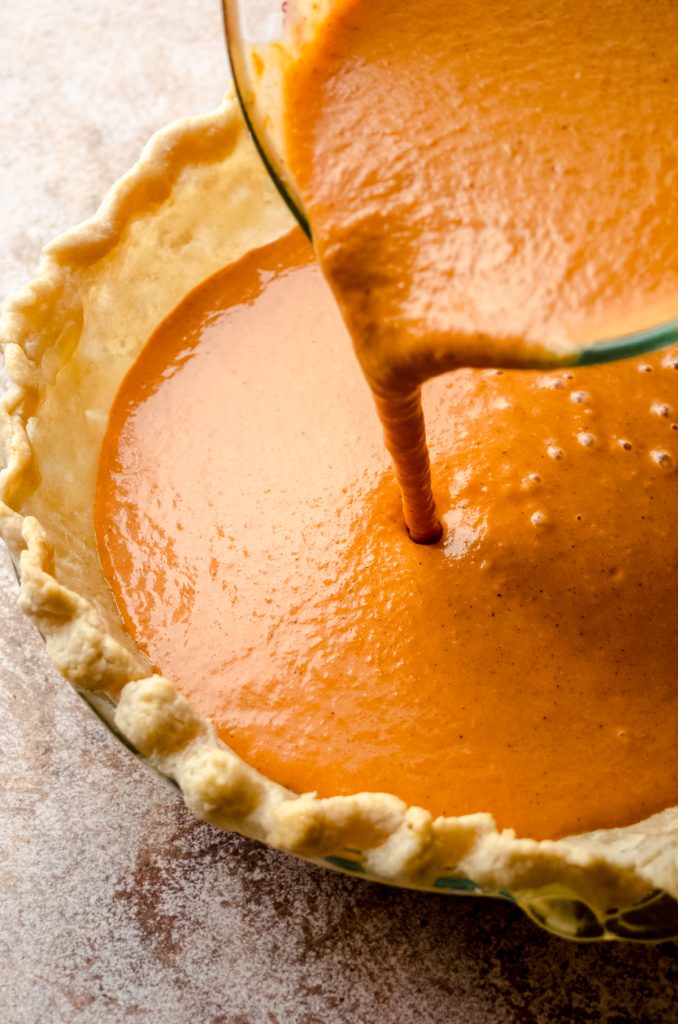 Someone is pouring pumpkin pie filling into a blind baked pie crust.