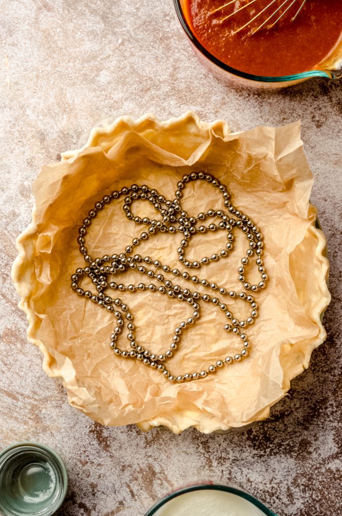 Aerial photo of a pie plate filled with parchment paper and pie weights to blind bake the crust.