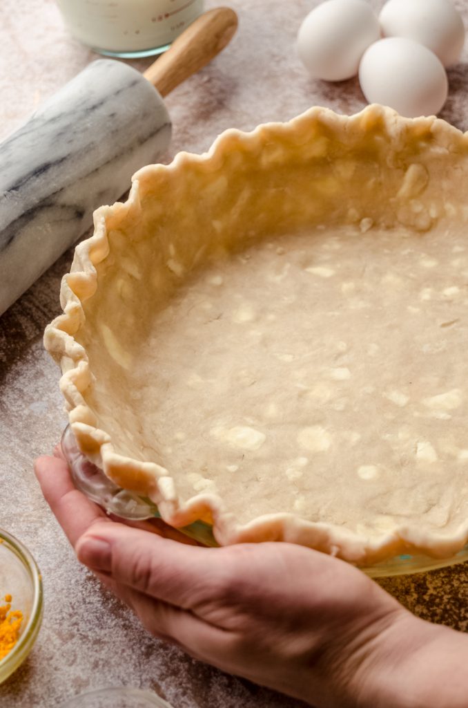 A photo of someone's hands placing a pie plate lined with a pie crust on a surface.