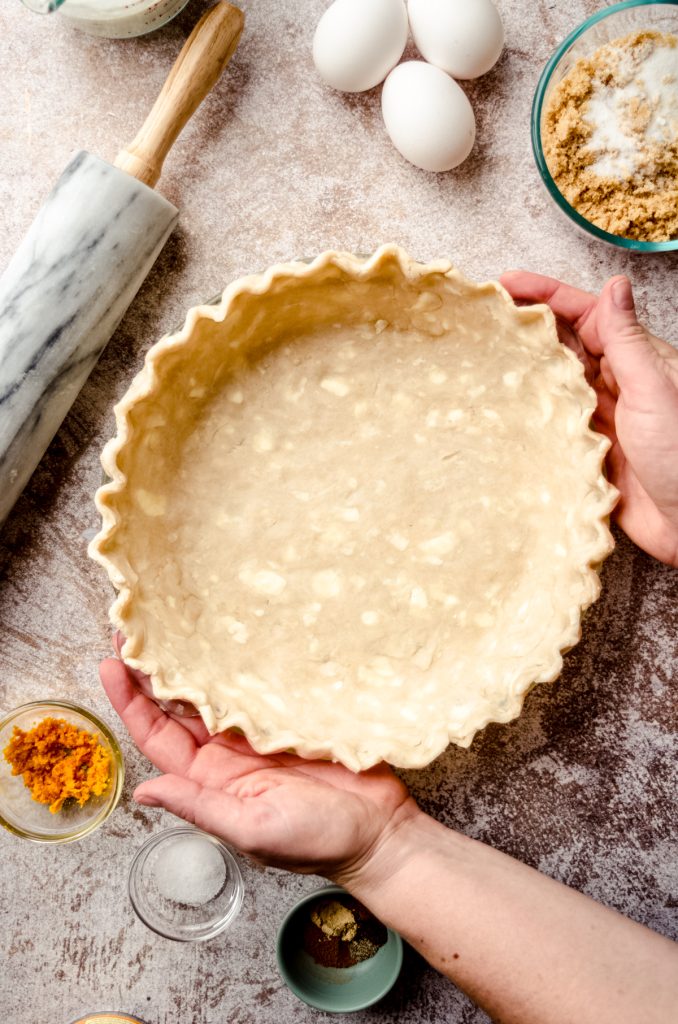 Aerial photo of someone placing a pie plate lined with a pie crust on a surface.