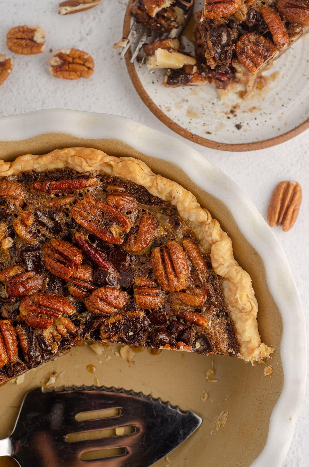 aerial photo of chocolate chip pecan pie with some slices missing and a pie server sitting in the pie plate