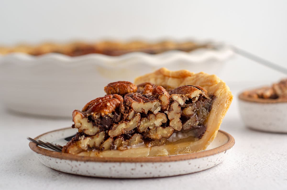 side view of a slice of chocolate chip pecan pie sitting on a plate