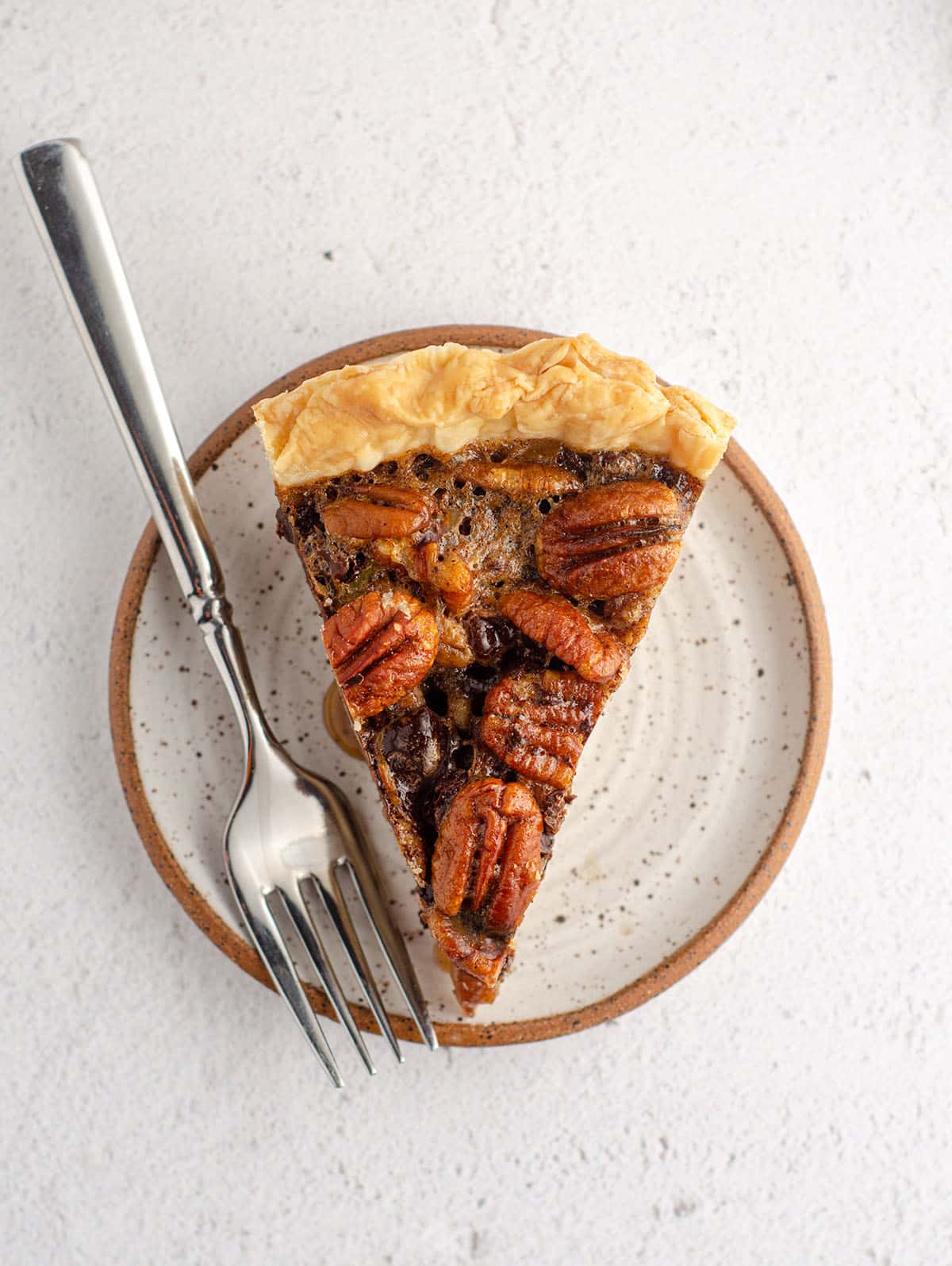 aerial photo of slice of chocolate chip pecan pie sitting on a plate with a fork