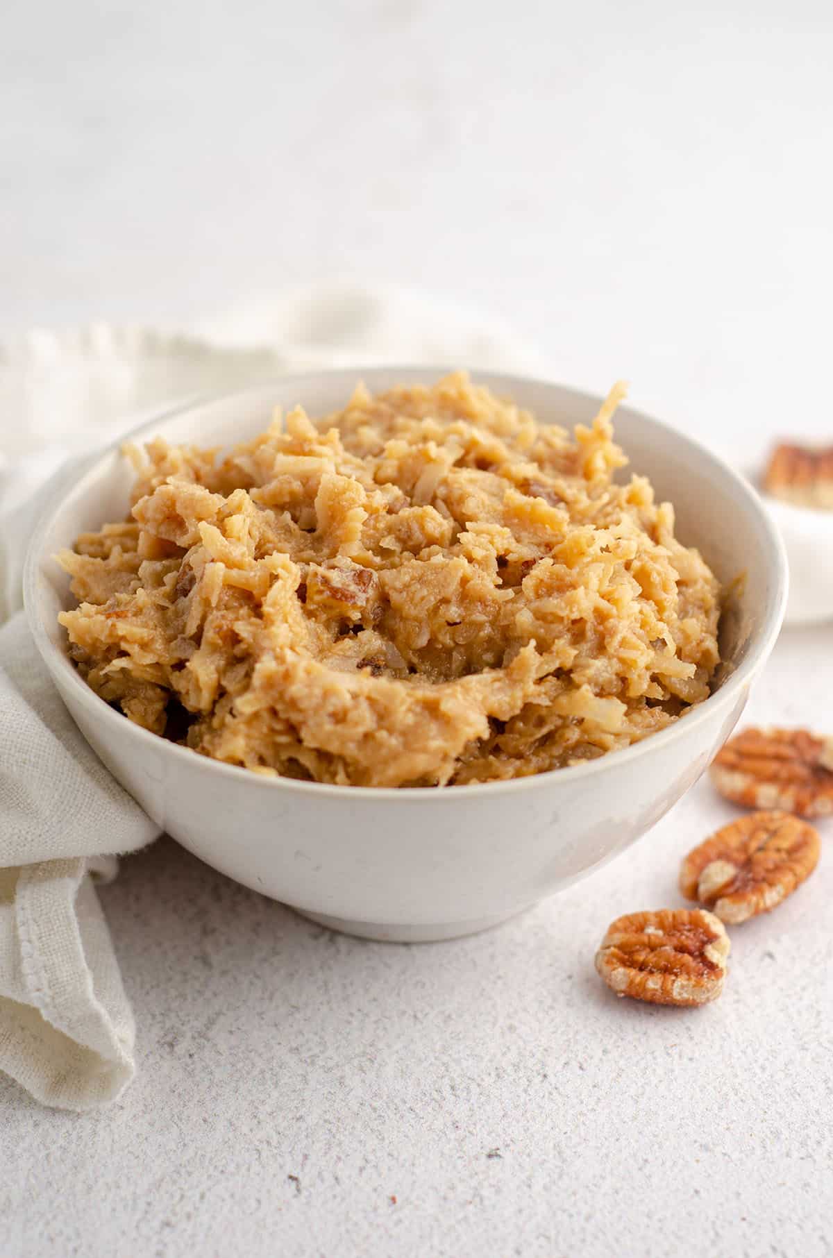 bowl of german chocolate frosting with pecans scattered around bowl