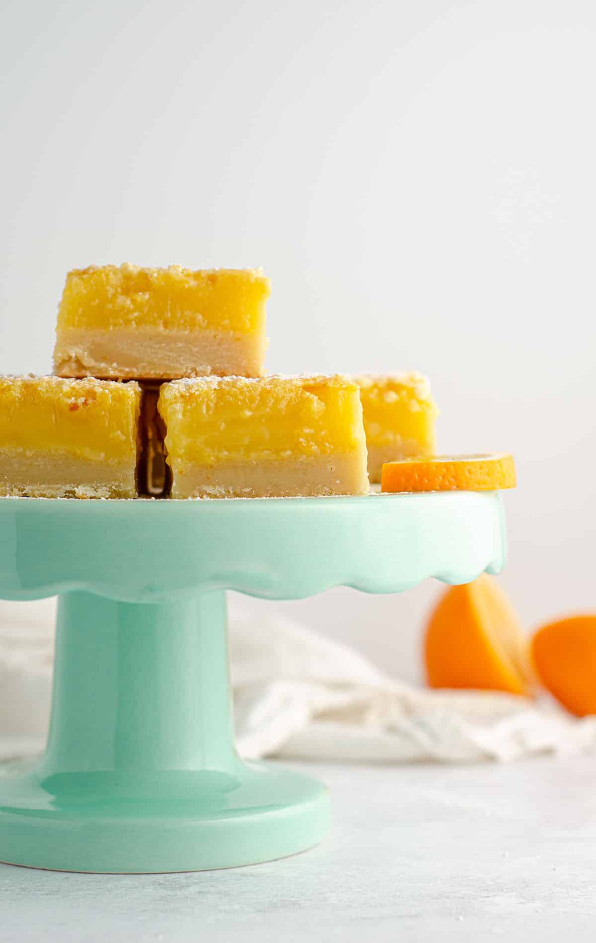 meyer lemon bars sitting on an aqua cake stand