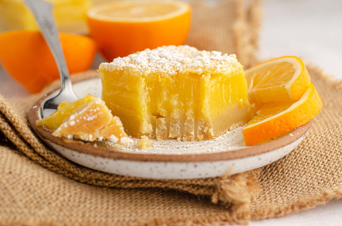 meyer lemon bar with a fork full taken out of it sitting on a plate with slices of meyer lemon