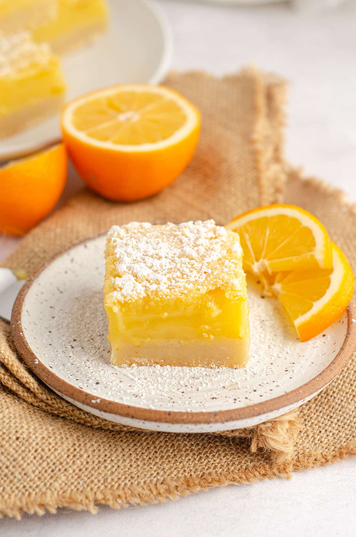 meyer lemon bar sitting on a plate with slices of meyer lemon