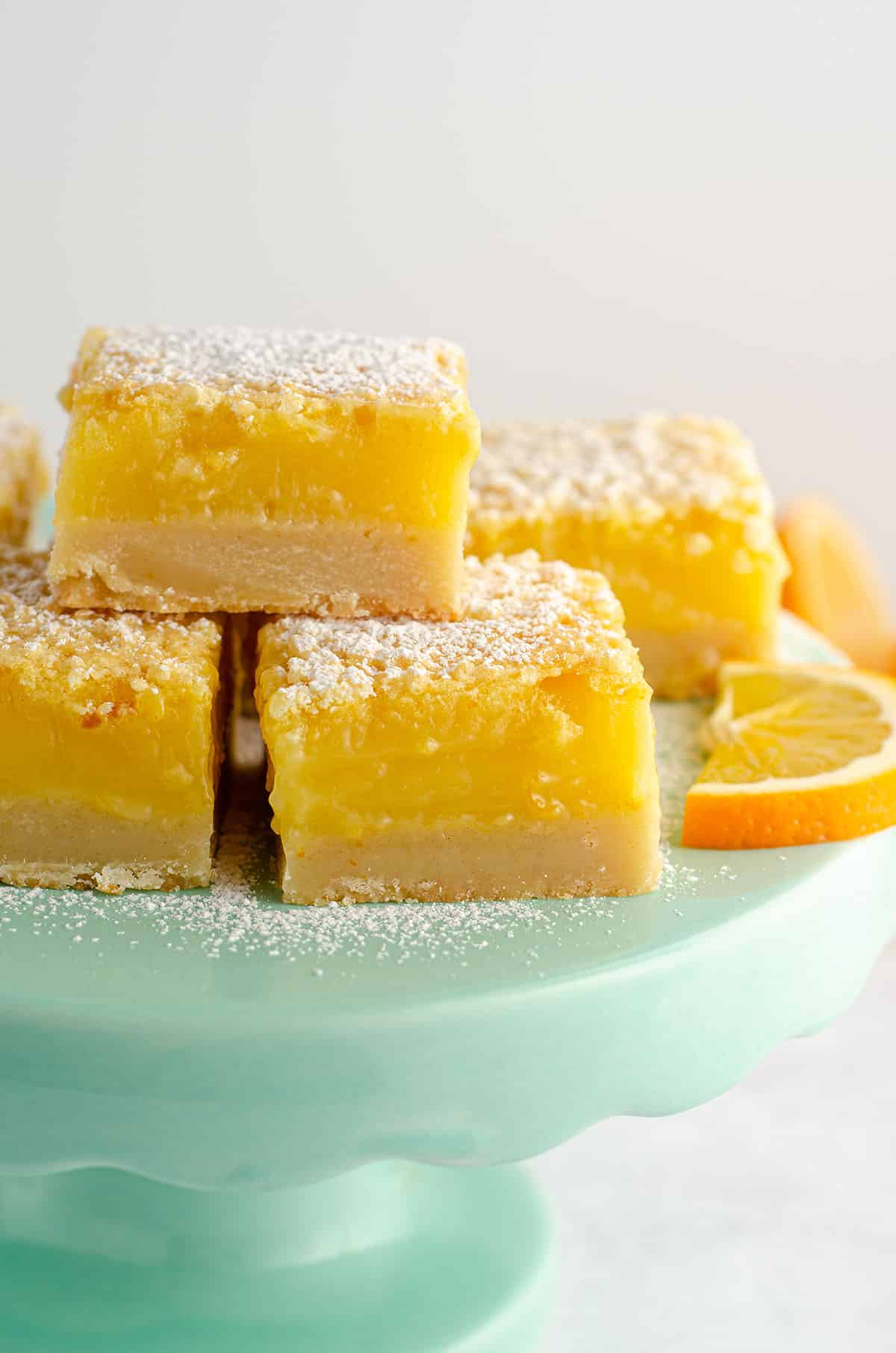 meyer lemon bars sitting on an aqua cake stand