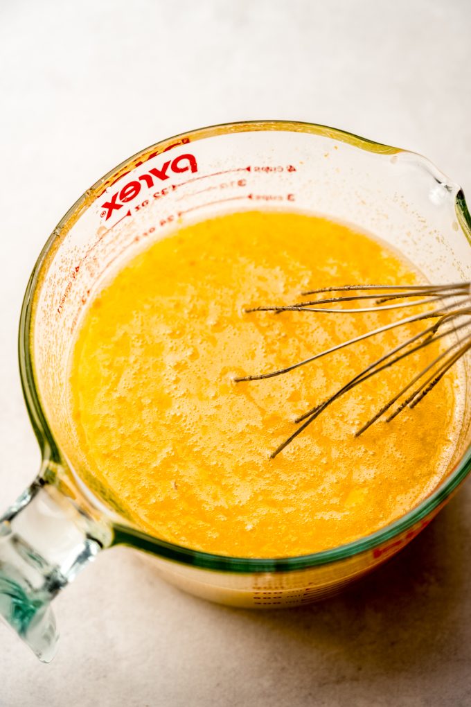 A large glass measuring cup filled with the filling mixture for Meyer lemon bars with a whisk in it.