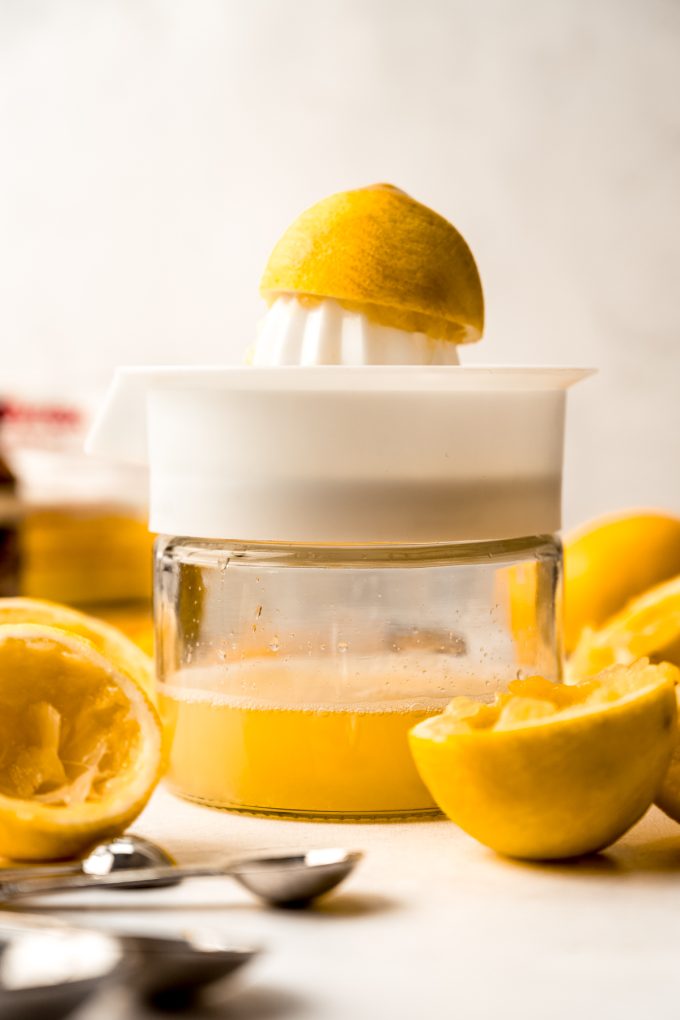 A juicer with half of a Meyer lemon on top of it with Meyer lemon juice in the canister.