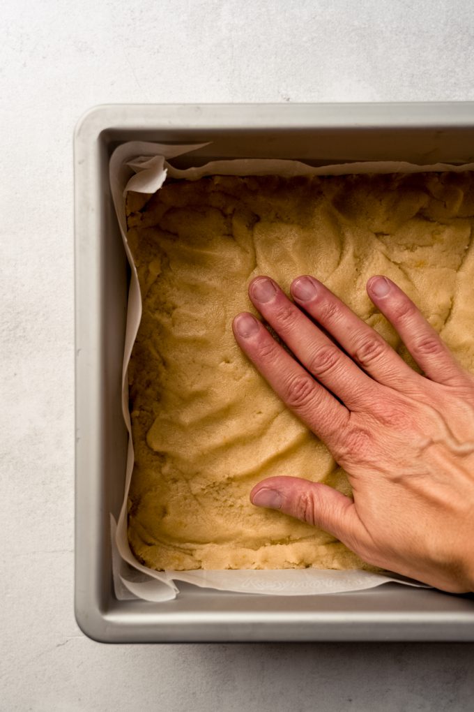 Someone is using their hand to press the crust into a baking pan for Meyer lemon bars.