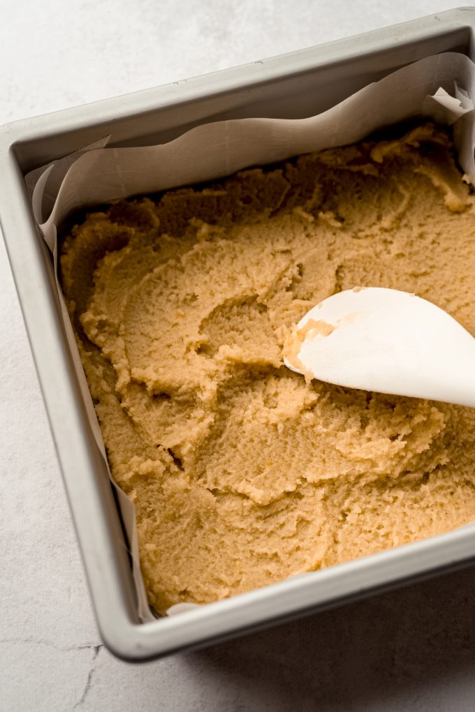 Someone is using a spatula to press the crust into a baking pan for Meyer lemon bars.