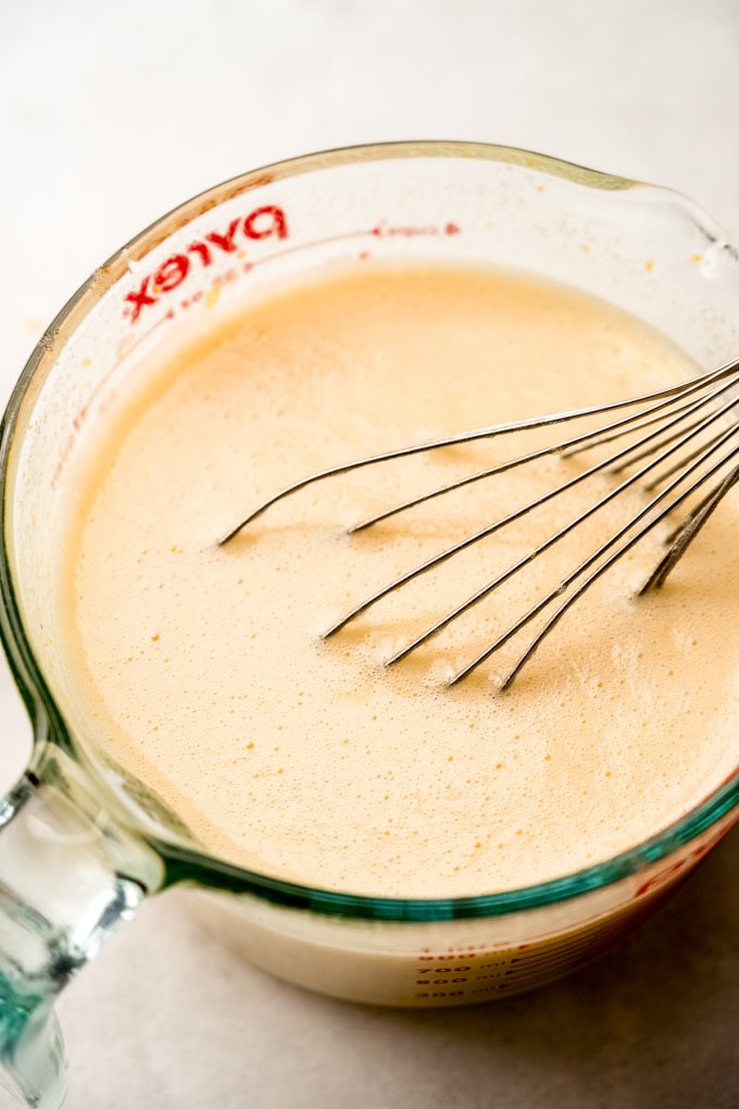A large glass measuring cup filled with the filling mixture for Meyer lemon bars with a whisk in it.
