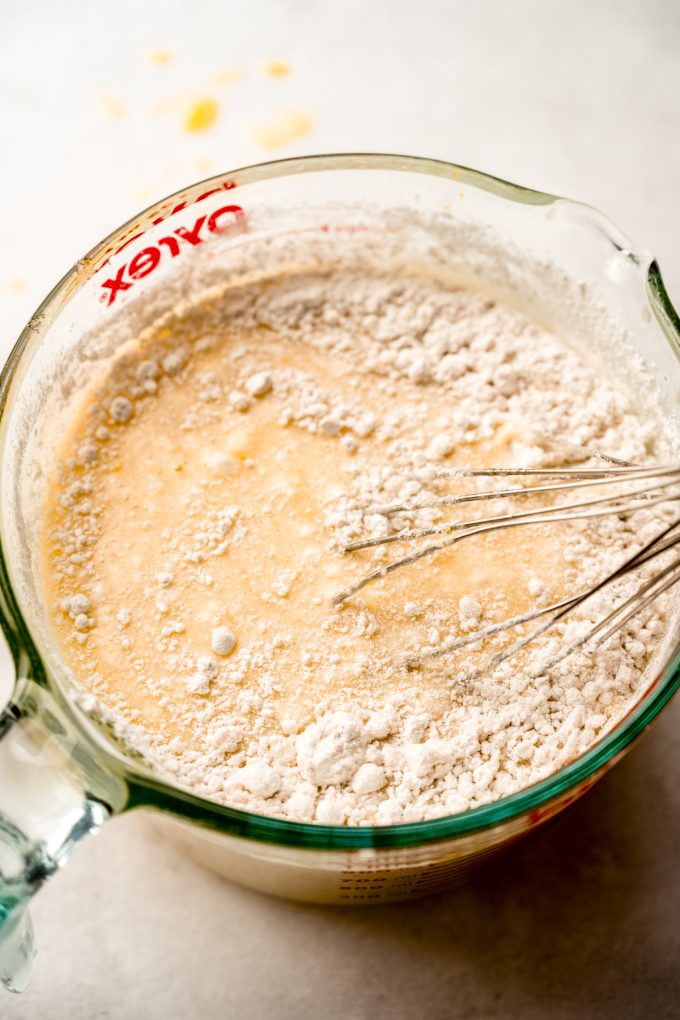 A large glass measuring cup filled with the filling mixture for Meyer lemon bars with a whisk in it.