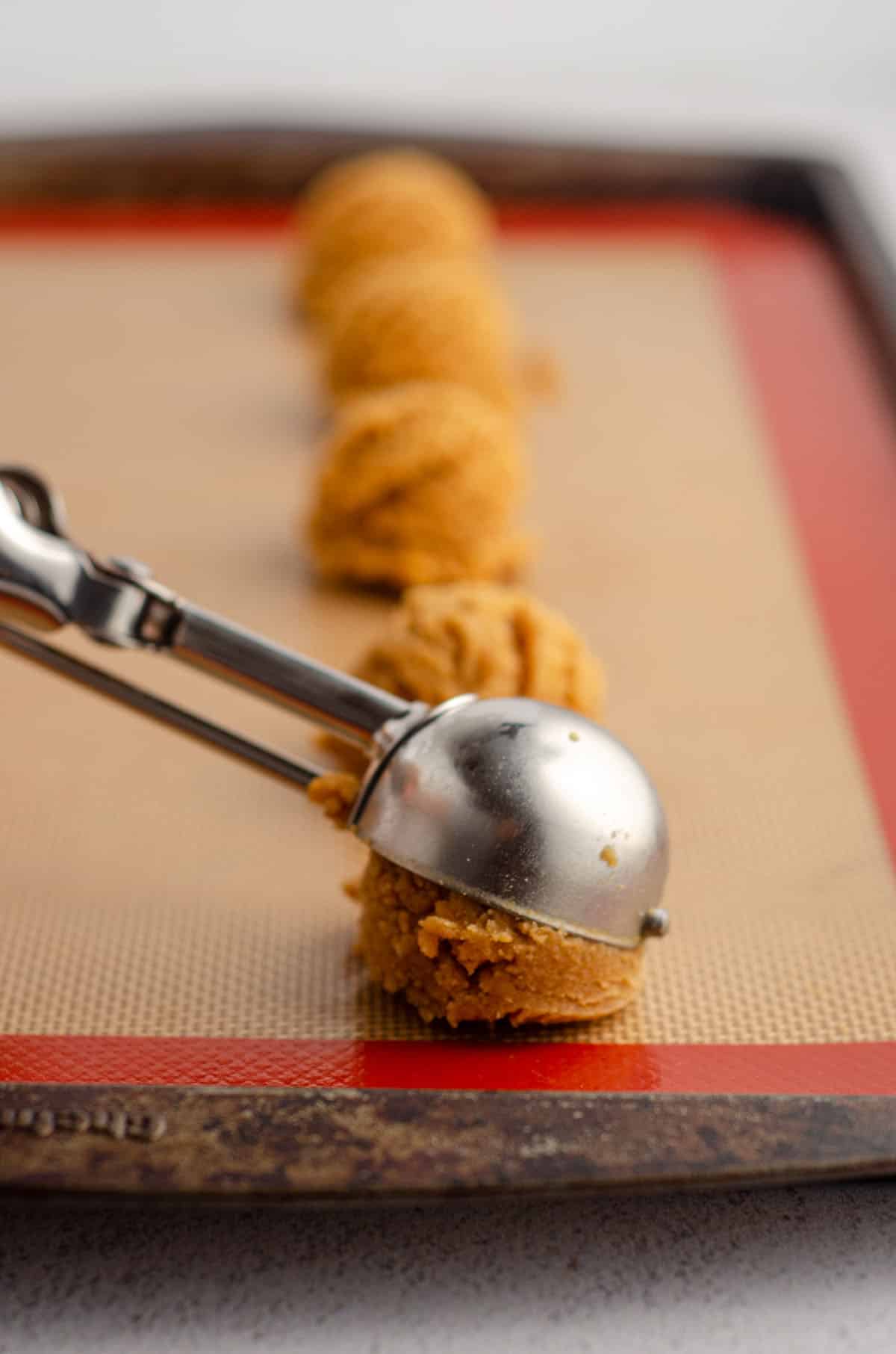 cookie scoop dropping peanut butter cookie dough onto a baking sheet