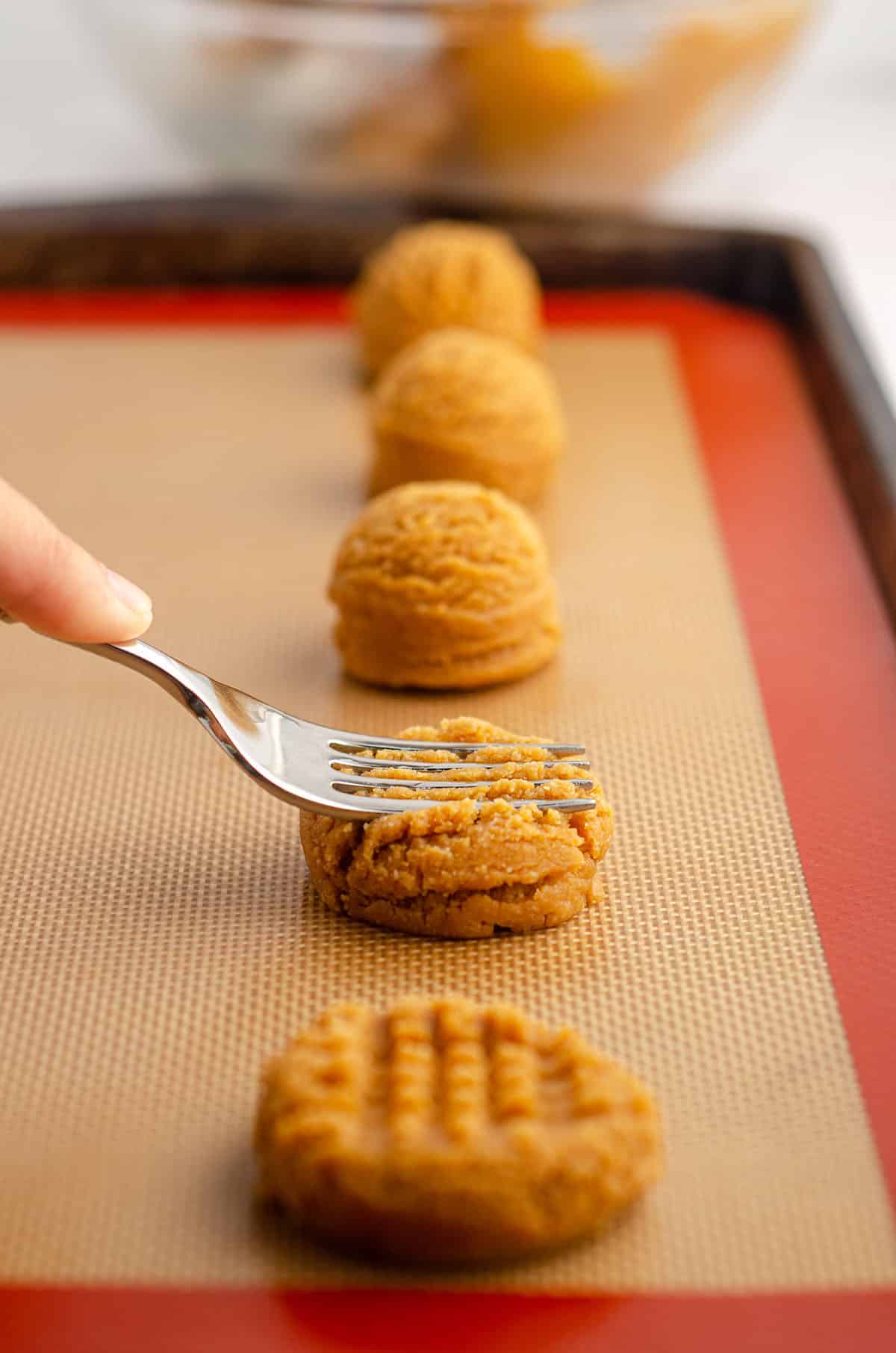 a hand using a fork to make crisscross pattern on peanut butter cookies