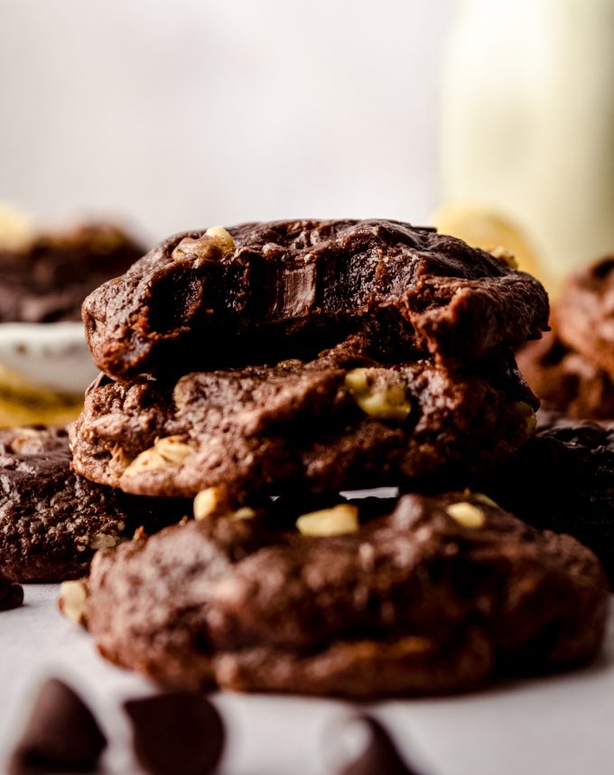 A stack of brownie cookies on a surface and a bite has been taken out of the one on the top.