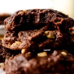 A stack of brownie cookies on a surface and a bite has been taken out of the one on the top.