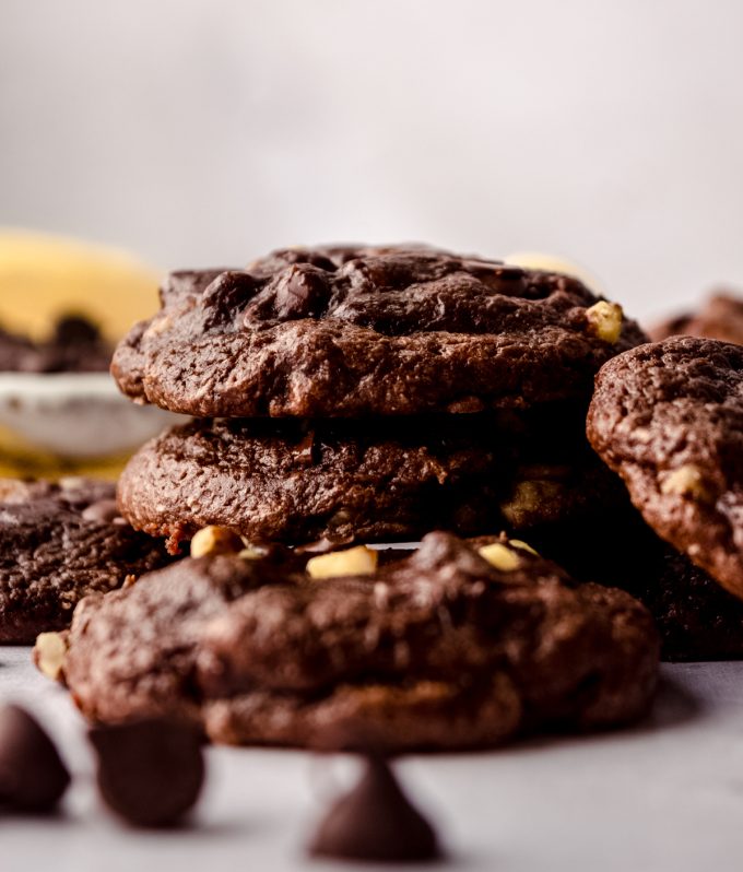 A stack of brownie cookies on a surface with chocolate chips in the foreground.