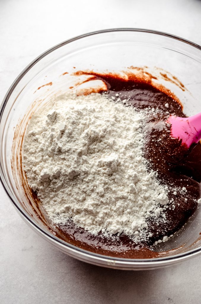 A bowl of flour and chocolate mixture to make brownie cookies with a pink spatula in it.