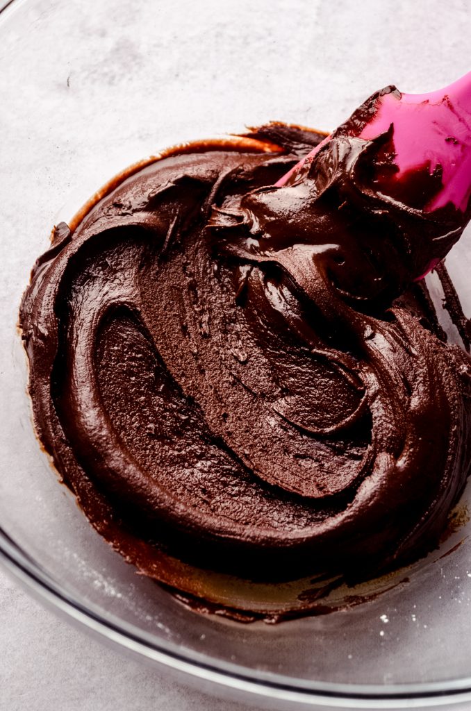 Aerial photo of a bowl of the melted chocolate mixture to make brownie cookies with a pink spatula in the bowl.