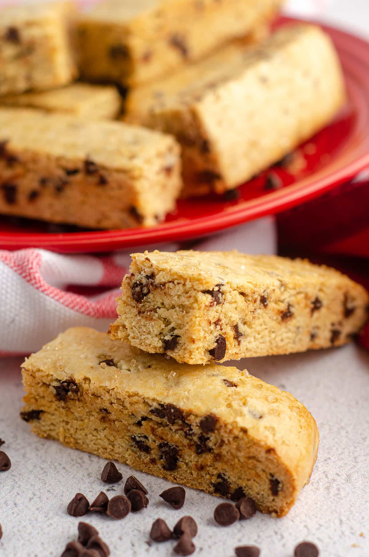 chocolate chip biscotti sitting on and in front of a red plate with mini chocolate chips scattered around
