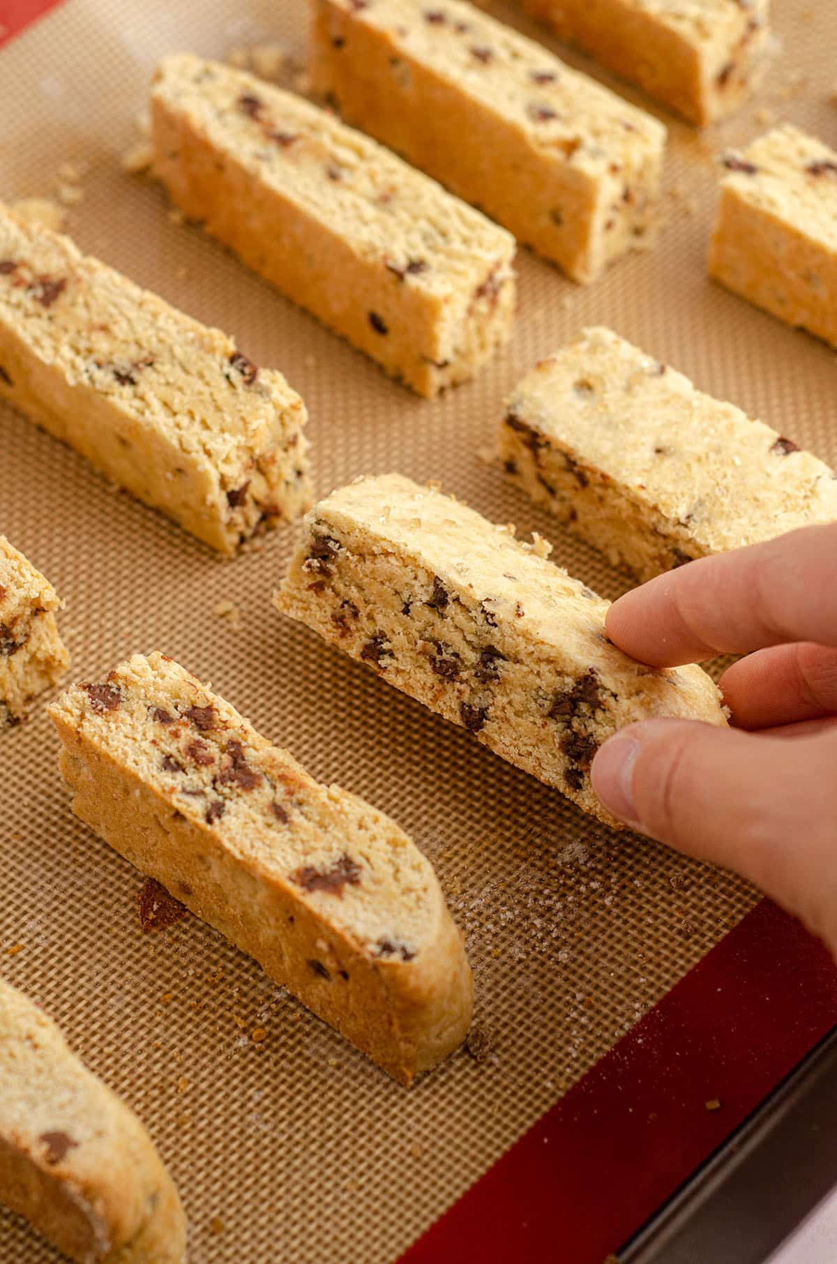 hand turning chocolate chip biscotti over on baking sheet to bake
